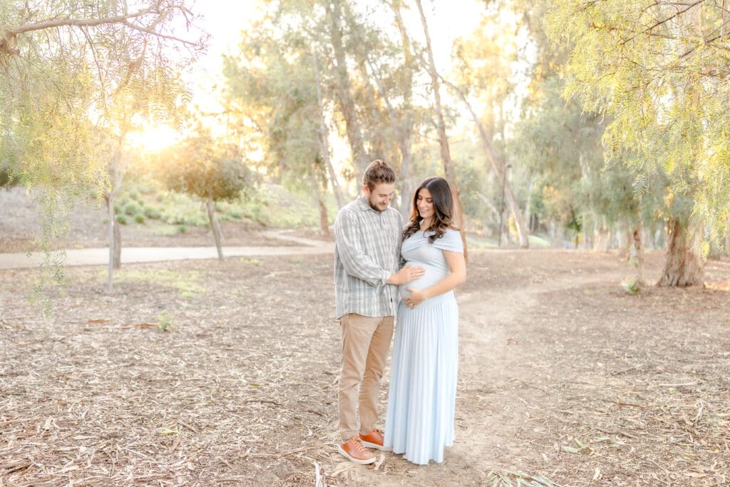 a husband and wife in a field looking down at their baby bump 