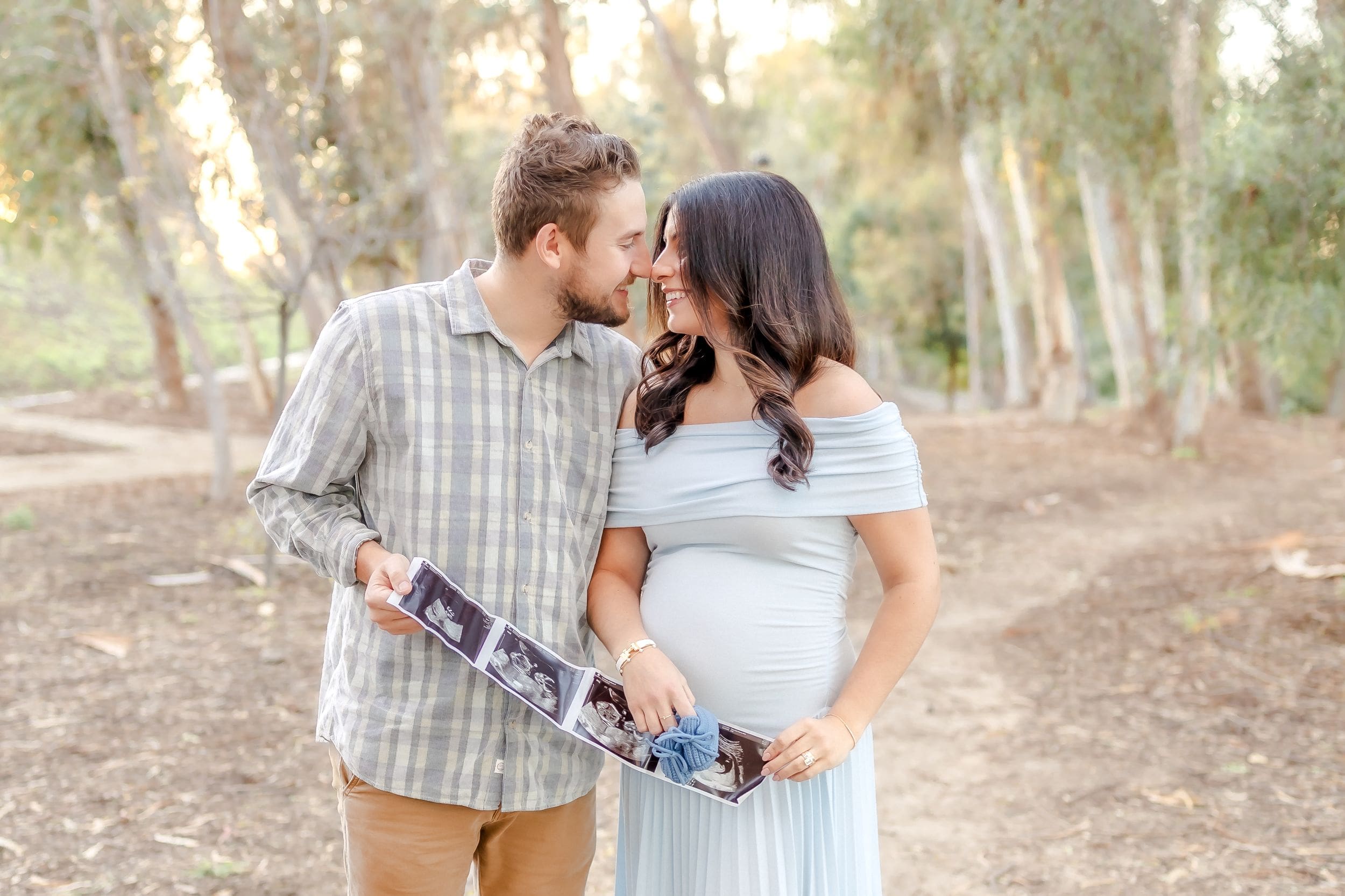 Couple embraces lovingly during outdoor photoshoot in wooded area with soft natural lighting.