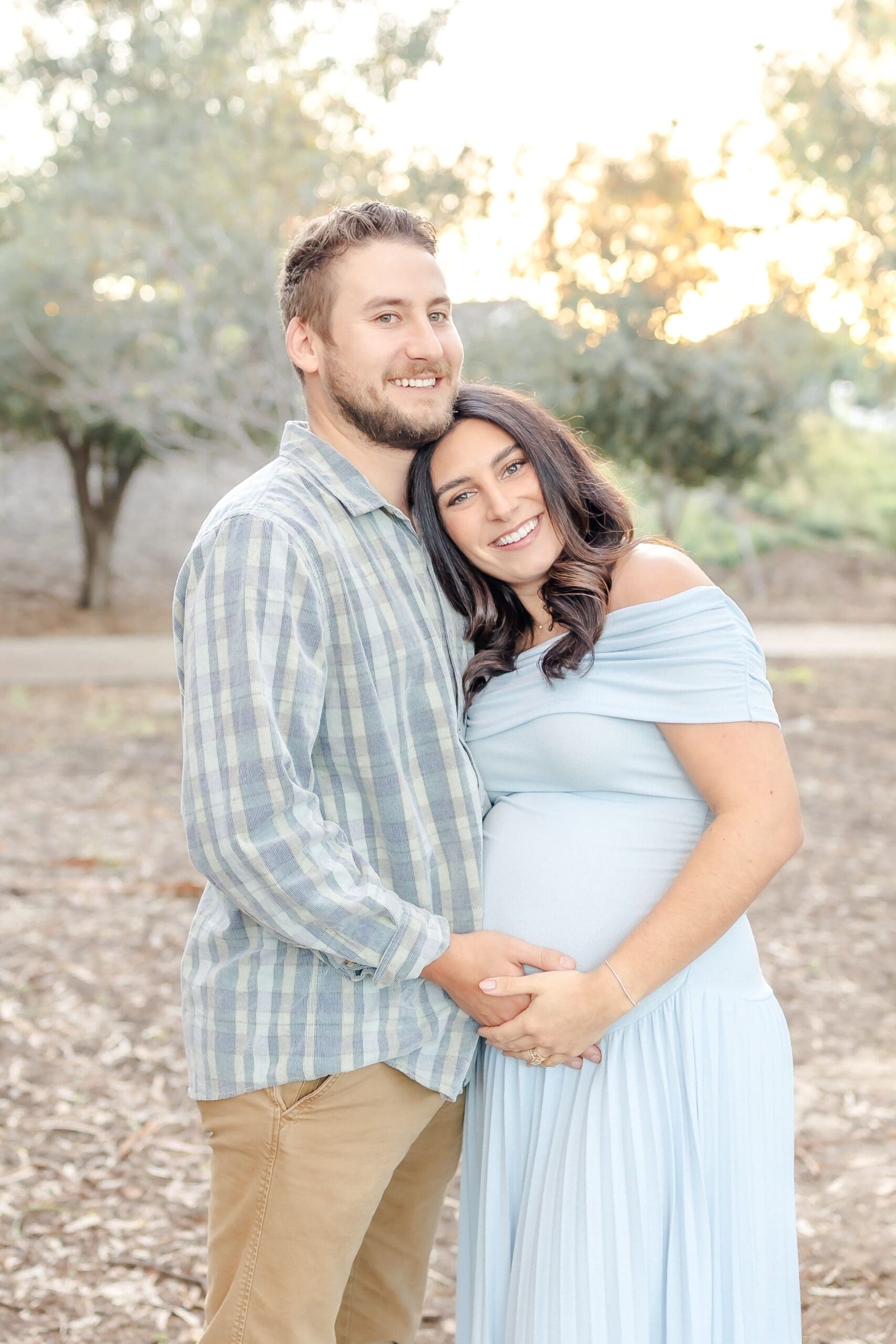 A couple in light blue and plaid share tender moments during a romantic outdoor photoshoot in a natural setting.
