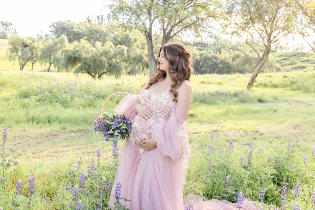 A mother in a lupine field with her eyes closed during her maternity session with Erin Custer Photo 