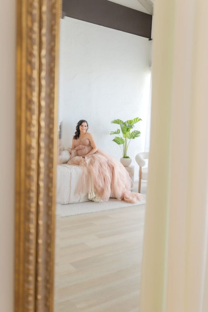 Expecting mother sitting on white linen bed, glowing natural light maternity portrait