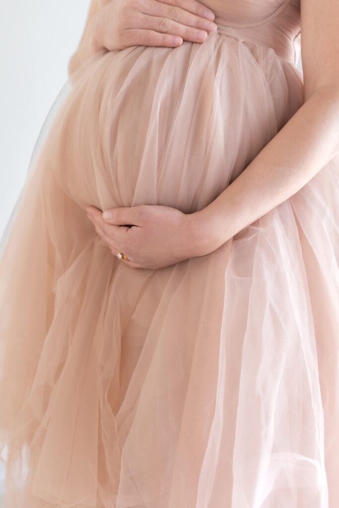 Close-up of pregnant belly wrapped in cream fabric, fine art maternity detail shot
