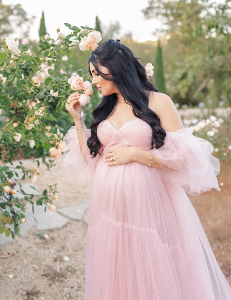 Summer maternity session in a rose garden with mom smelling flowers