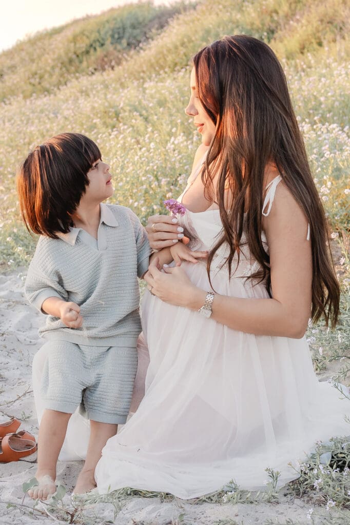 pregnant mom in a white flowing gown getting flowers from her toddler 