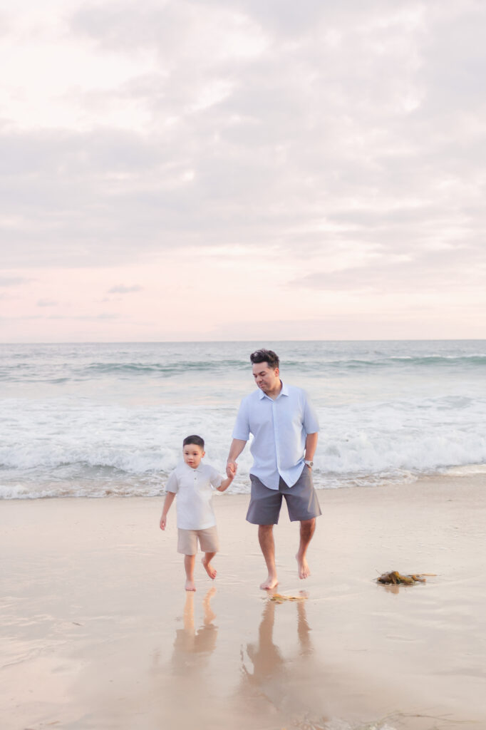 Dad and son holding hands as the sun sets over Newport Beach during a summer photo session.