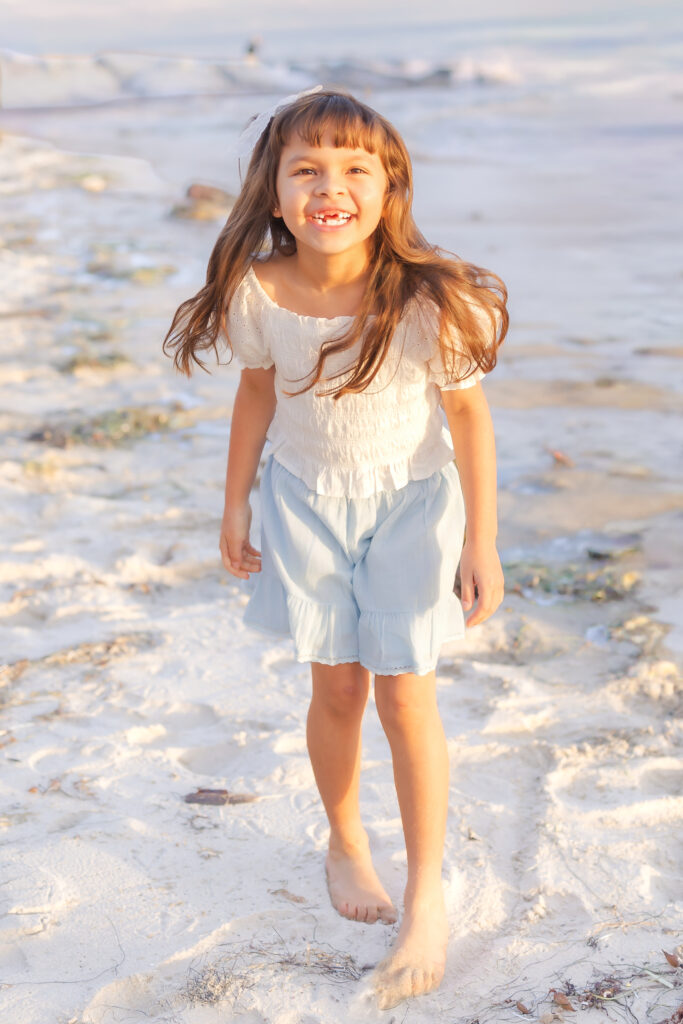 Young children running barefoot through the sand during a Newport Beach summer family photo session.
