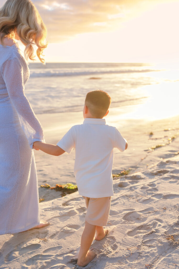 Mother holding her sons hand while watching the sunset during a Newport Beach summer photography session.